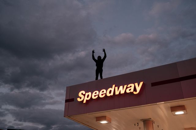 A man standing atop a gas station with his arms up during a protest